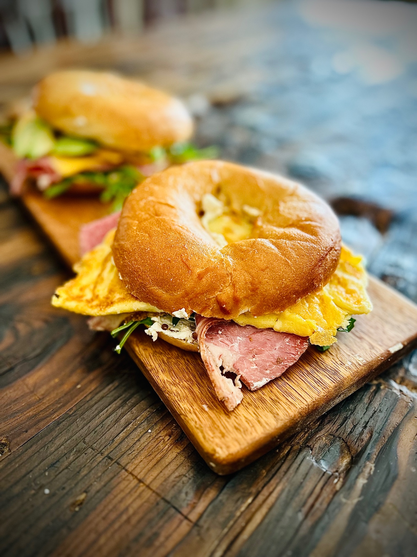 Bagel with ham, omelette and rocket on wood board